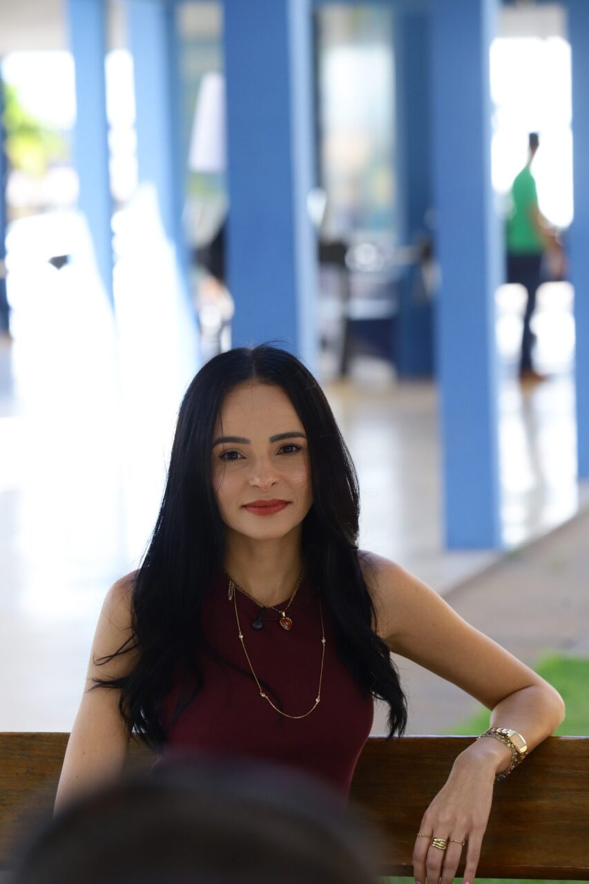Retrato de uma mulher jovem, de cabelo longo e escuro solto, sorrindo para a câmera.