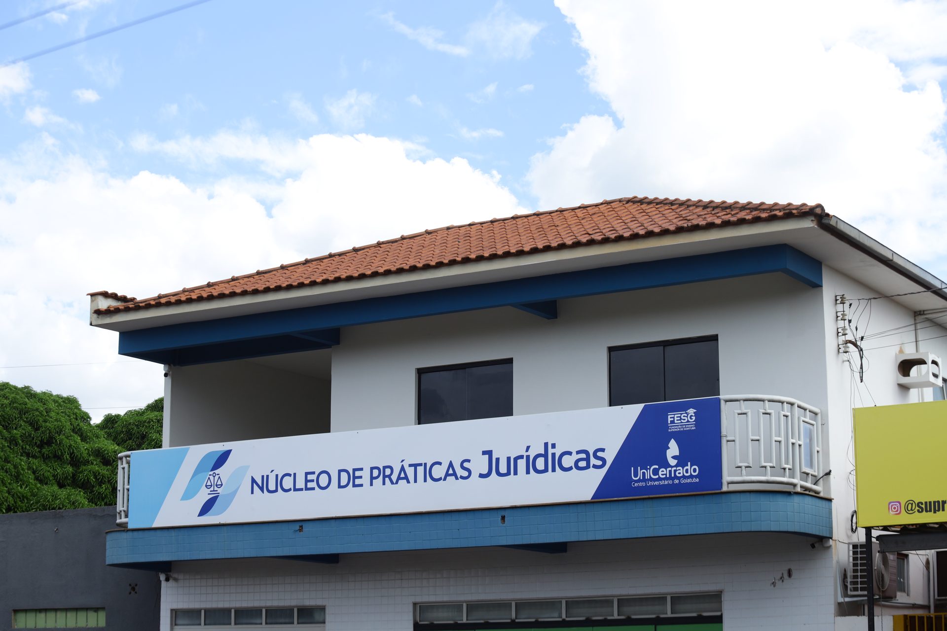 Fachada de prédio de dois pavimentos com telhado de telhas cerâmicas, paredes brancas e detalhes em azul.