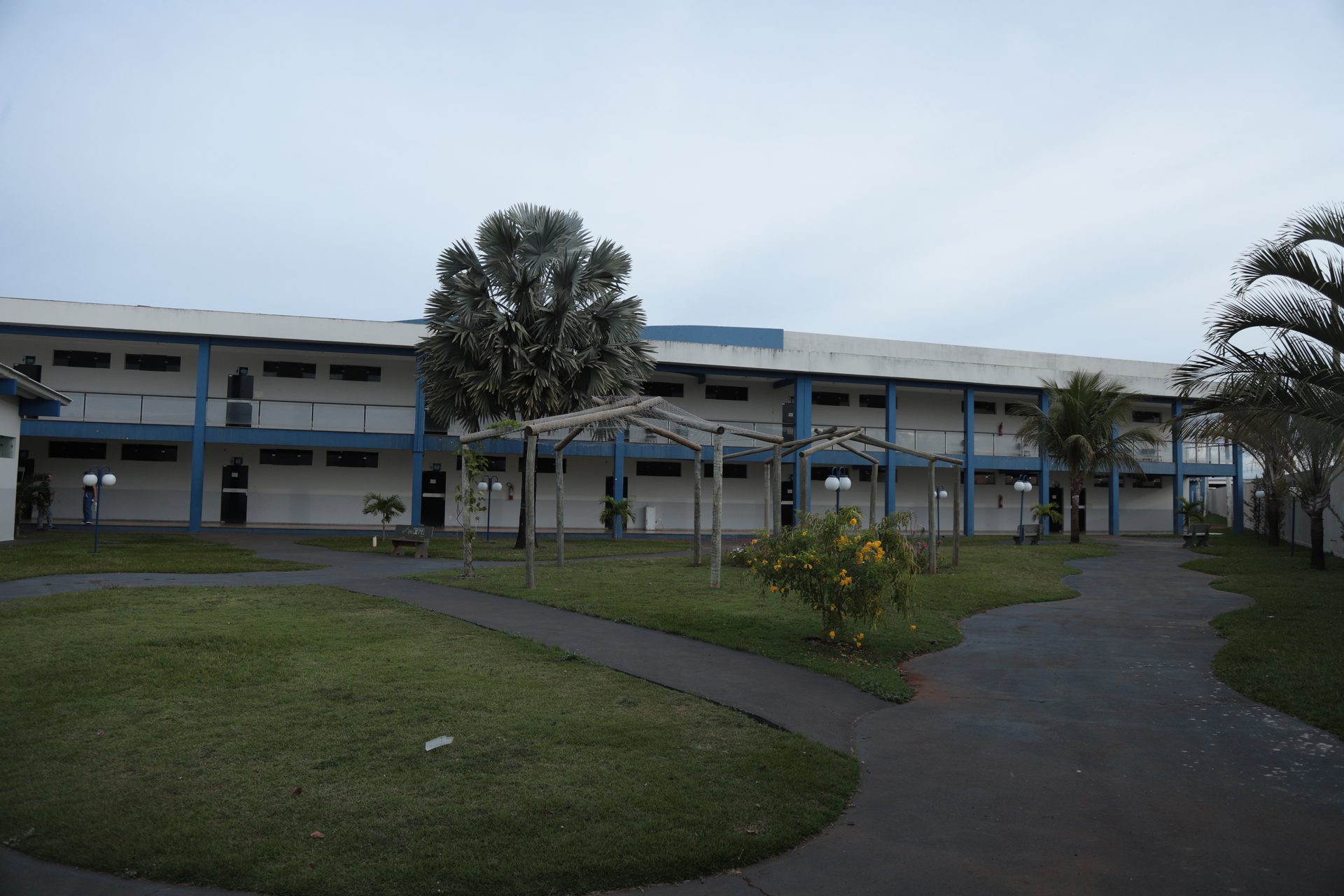 Fachada de prédio institucional de dois pavimentos, com estrutura branca e detalhes em azul, varandas com guarda-corpo e diversas janelas.
